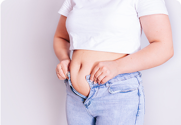 Woman standing and unbuttoning her jeans, highlighting bloating and abdominal weight gain related to cortisol and hormonal imbalance.
