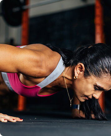 Focused woman performing push-ups in a gym, representing strength, confidence, and muscle preservation supported by hormone therapy.