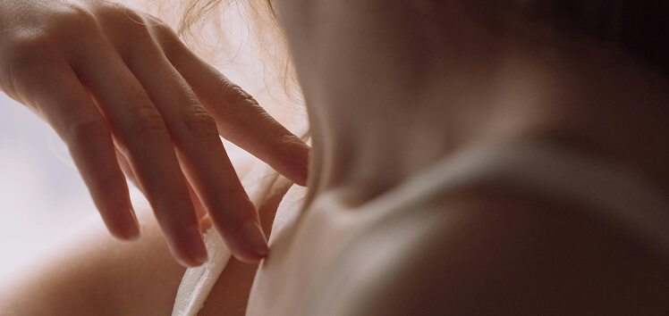 Woman resting her hand on her neck in warm lighting, symbolizing how testosterone testing supports energy, mood, and skin health.