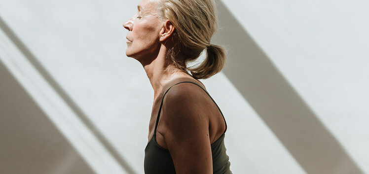 Mature woman in a black tank top standing in sunlight with eyes closed, representing how DHEA-S testing helps assess adrenal function, aging, and hormone balance.