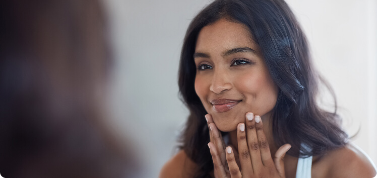 Mature woman smiling while applying skincare in front of a mirror, representing how LH and FSH hormone testing supports women’s reproductive health, skin vitality, and confidence through menopause.