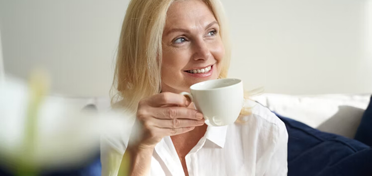 Smiling woman holding a cup of coffee in natural light, representing how insulin testing helps identify resistance and support metabolic and hormonal health.
