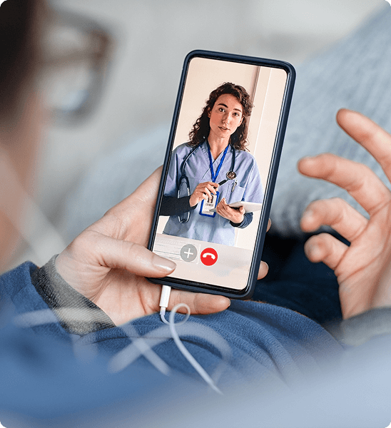 A person has a telehealth video call on their smartphone with a female doctor in blue scrubs.