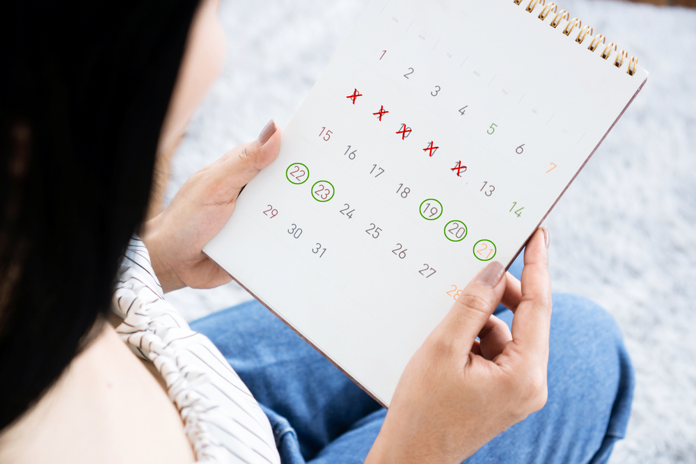 Asian woman hand holding calendar counting the date and checking her menstrual cycle planning for ovulation  