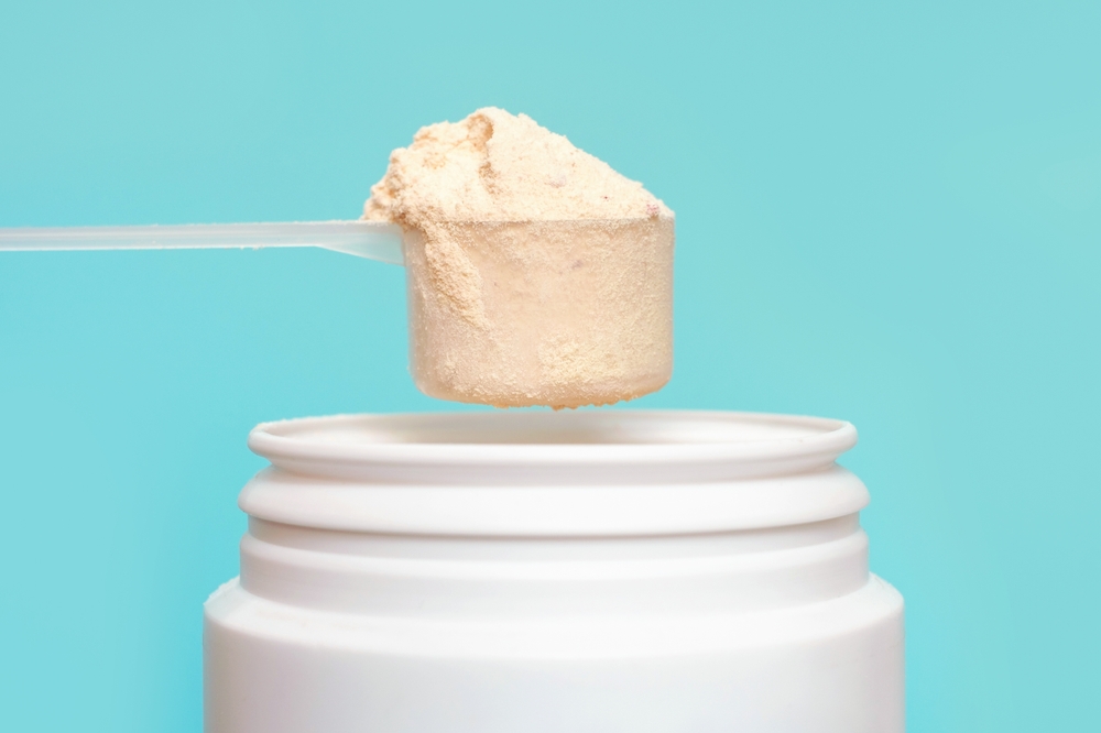 Protein-powder-in-scoop-and-plastic-jar-on-blue-background