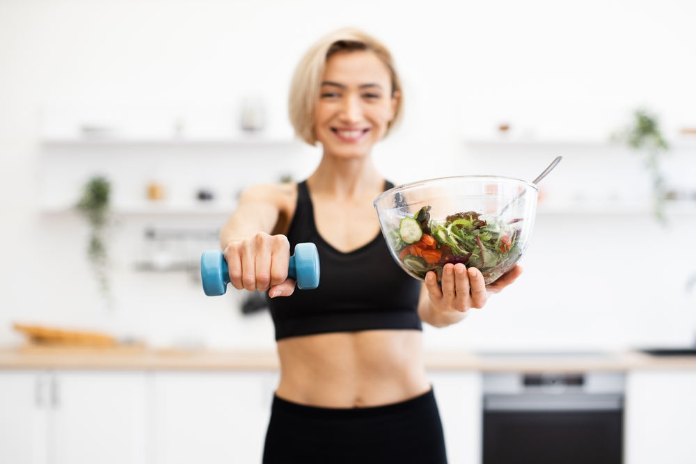 Woman promoting healthy lifestyle with fresh salad and dumbbell