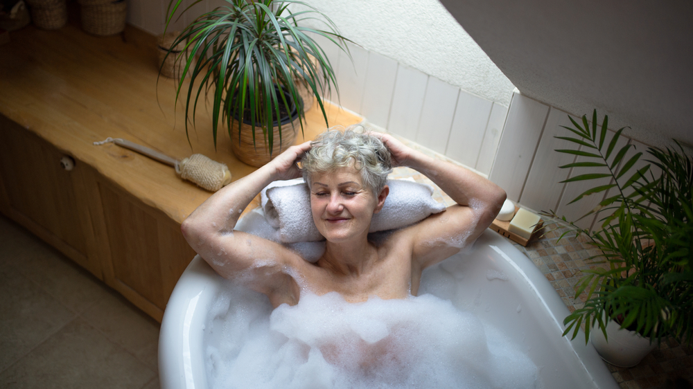 Top view of relaxed senior woman lying in bath tub at home