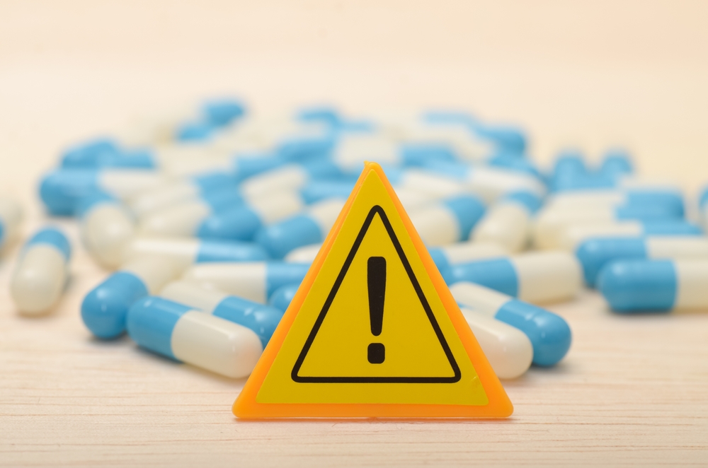 black exclamation mark on yellow triangle with blue and white pills in the background side effects concept