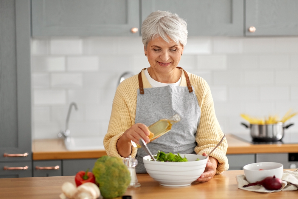 happy smiling senior woman with olive oil making vegetable salad in her kitchen
