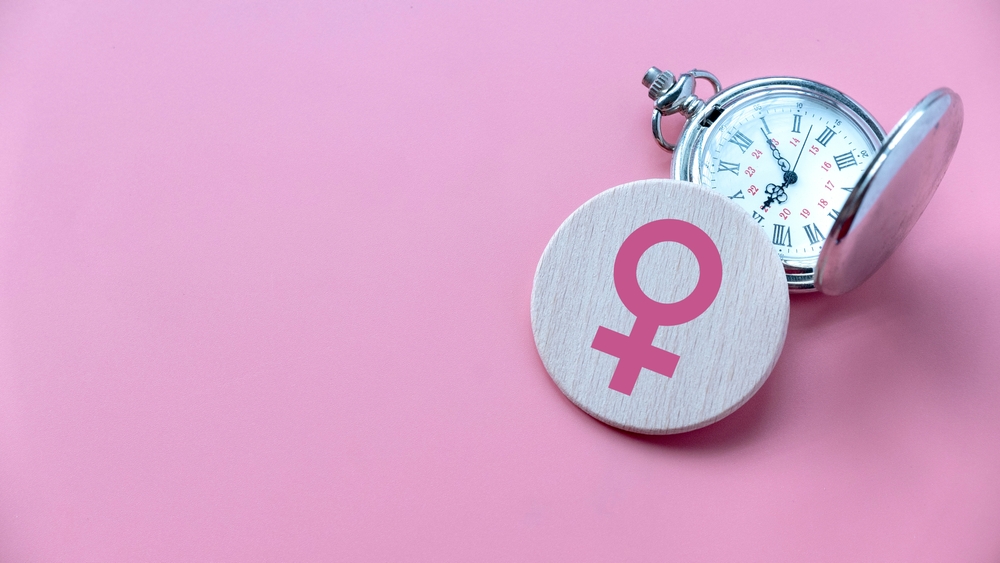 Menopause concept female symbol over a watch on Pink background