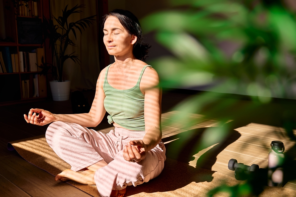 cortisol-and-weight-gain-Woman-practicing-yoga-and-meditation-at-home-sitting-in-lotus-pose-on-yoga-mat-relaxed-with-closed-eyes